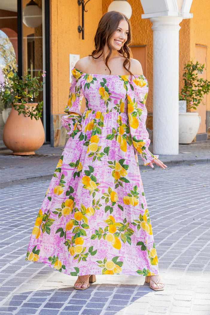 Woman in a floral dress standing in front of architectural columns with a yellow wall and plants in the background.